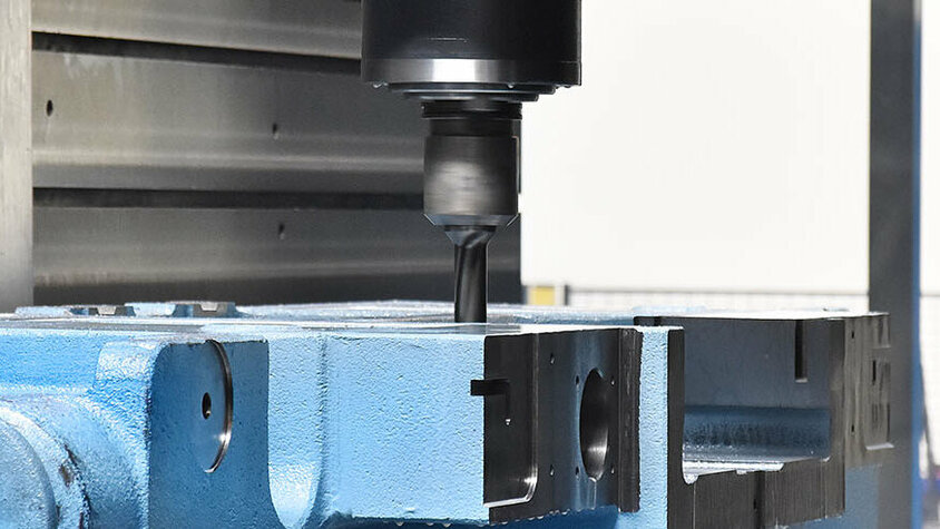 Nahaufnahme eines Fräsvorgangs in der mechanischen Bearbeitung. Ein CNC-Fräswerkzeug bearbeitet präzise ein blaues Metallwerkstück. Die Drehbewegung des Fräskopfes und die Einspannung des Werkstücks deuten auf einen hochpräzisen Bearbeitungsprozess hin. Der Hintergrund zeigt die kontrollierte Umgebung innerhalb der CNC-Maschine, die für die Fertigung komplexer Metallteile optimiert ist.