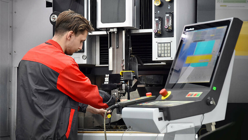 Das Bild zeigt einen Werkzeugbautechniker von weba Olomouc, der konzentriert eine moderne Erodiermaschine bedient. Seine Hände sind geschickt damit beschäftigt, die Maschine zu steuern.