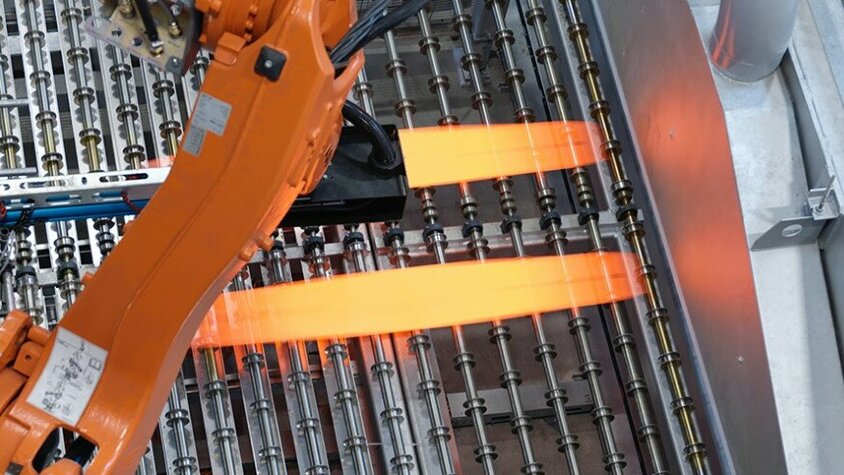 Industrieller Roboterarm in der Prozesstechnik für das Presshärten positioniert glühend heiße Metallbleche auf einer Produktionsanlage. Der Einsatz modernster Technologie optimiert den Presshärteprozess und gewährleistet eine präzise Steuerung der Umformprozesse bei weba Werkzeugbau.