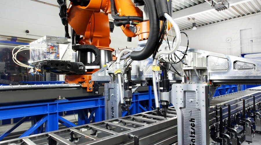 Ein moderner Industrieroboter in einer Produktionshalle, der an einer automatisierten Fertigungslinie arbeitet. Der Roboter führt Nieten und Clinchen durch, um Metallkomponenten präzise zu verbinden. Die Anlage ist an einer Förderanlage befestigt und befindet sich in einer hellen, industriellen Umgebung, die für effiziente und präzise Prozesse in der Fügetechnik steht.